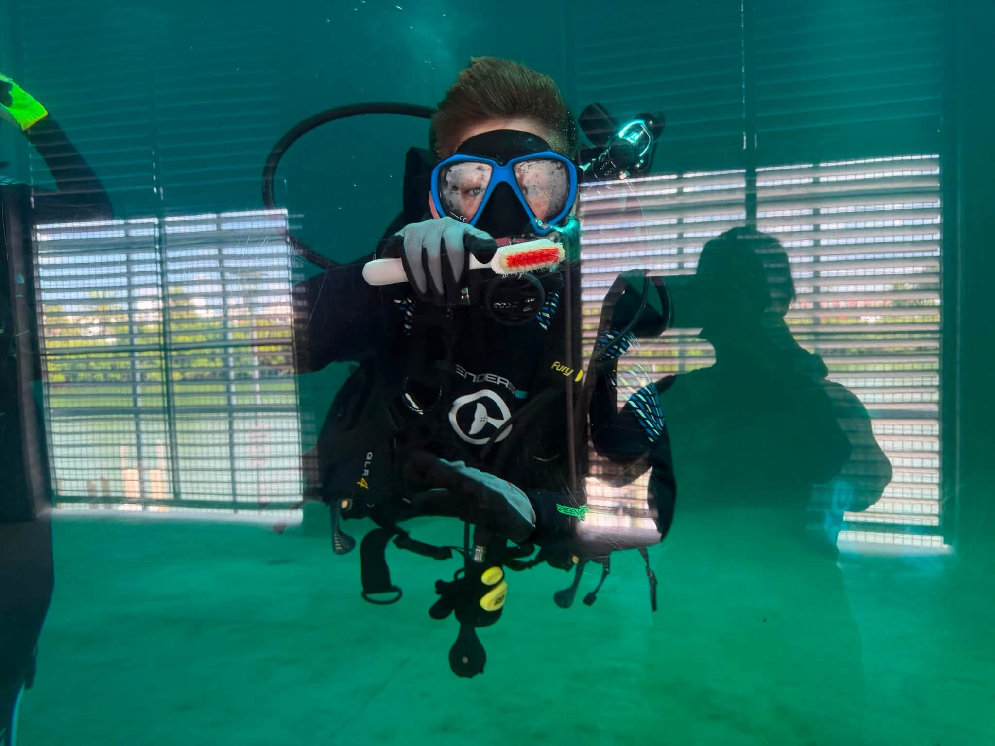 Jacob in scuba gear inside a CMA habitat, looking through the glass while holding a cleaning brush